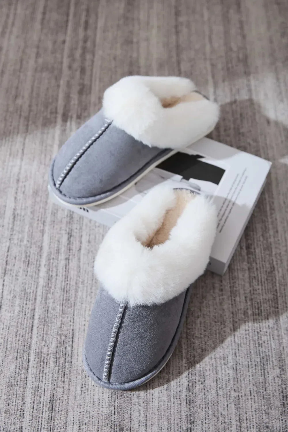 Pair of gray cozy slippers with white fluffy fur lining on gray carpet