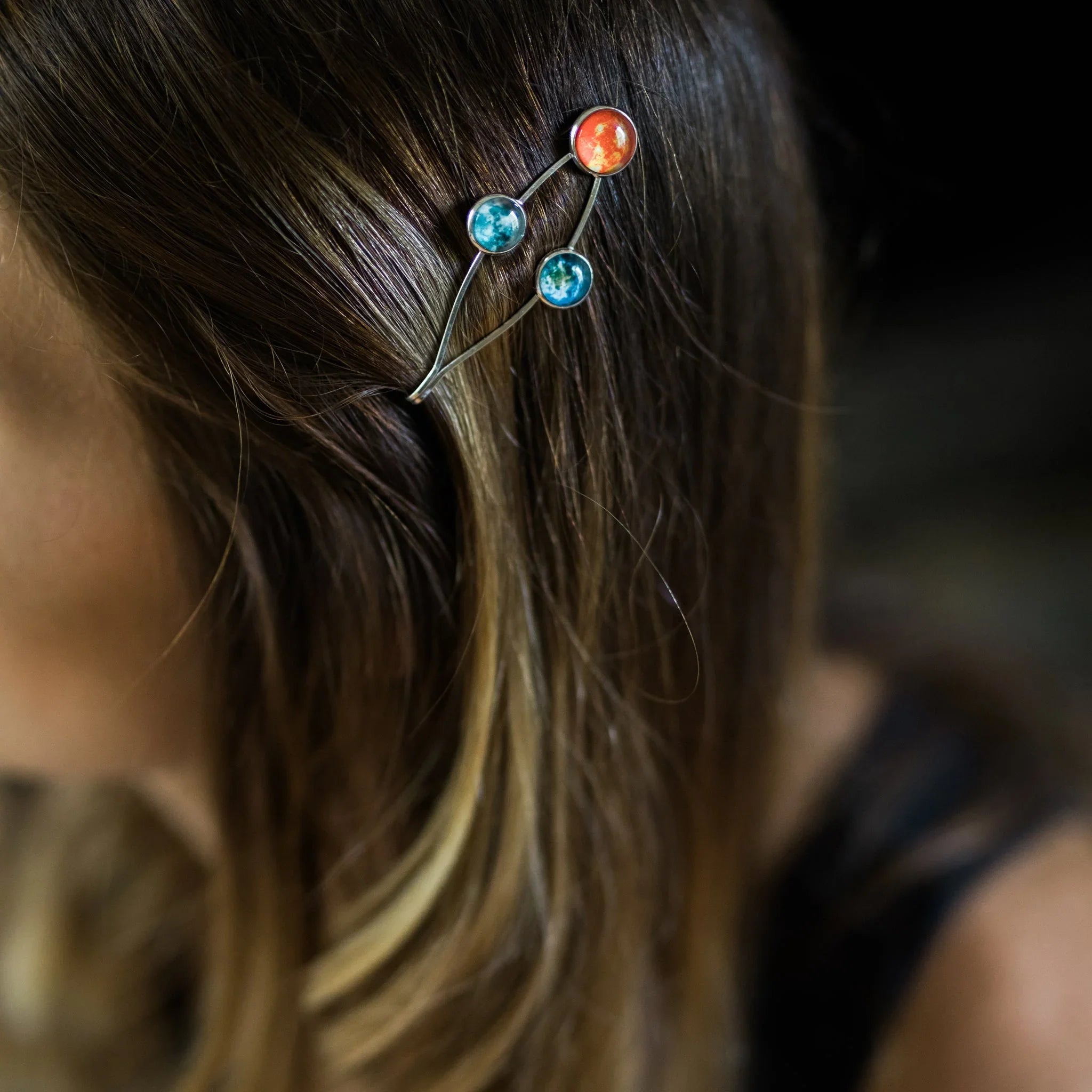 Close-up of hair with metal hairpin featuring three colorful planet charms in red and blue shades