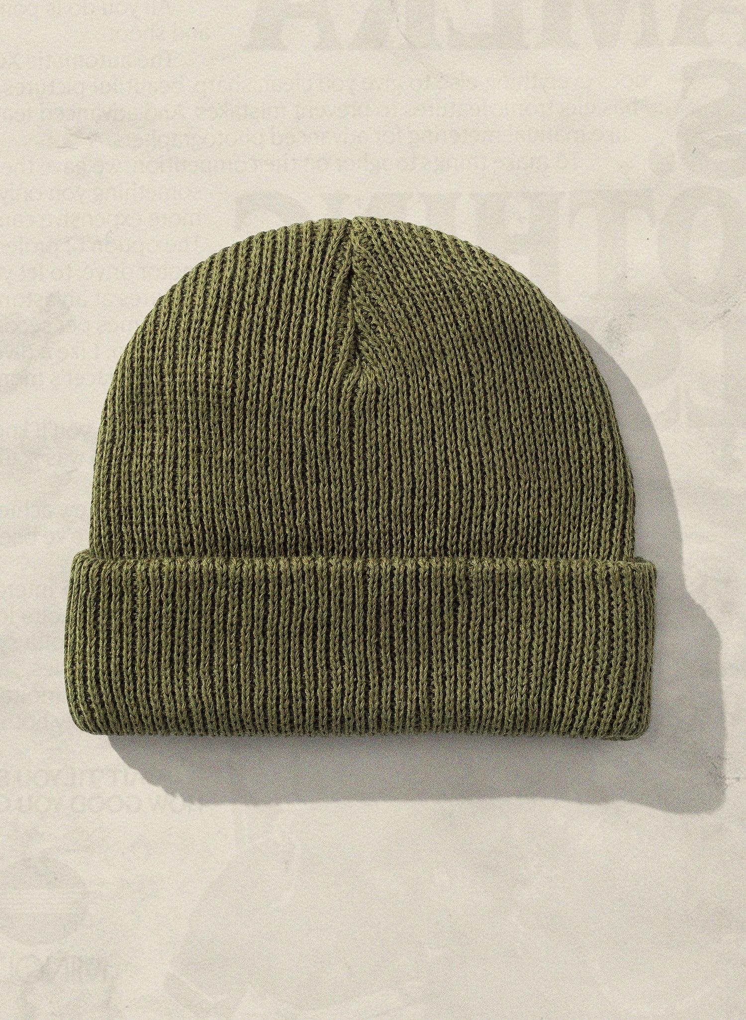 Olive green ribbed knit beanie hat with fold-up cuff, laid on a light neutral background