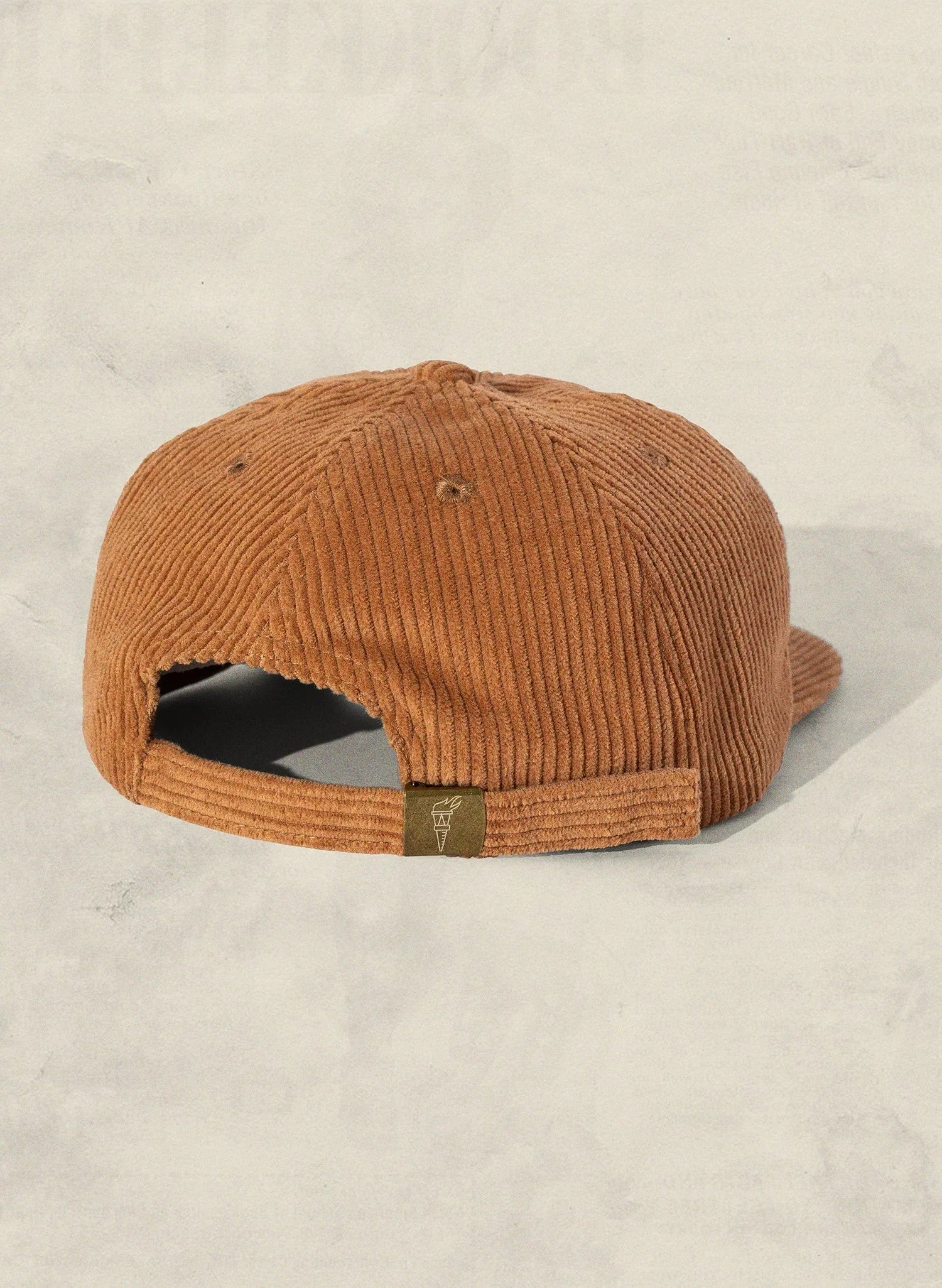 Brown corduroy baseball cap with adjustable back, displayed on a light textured surface