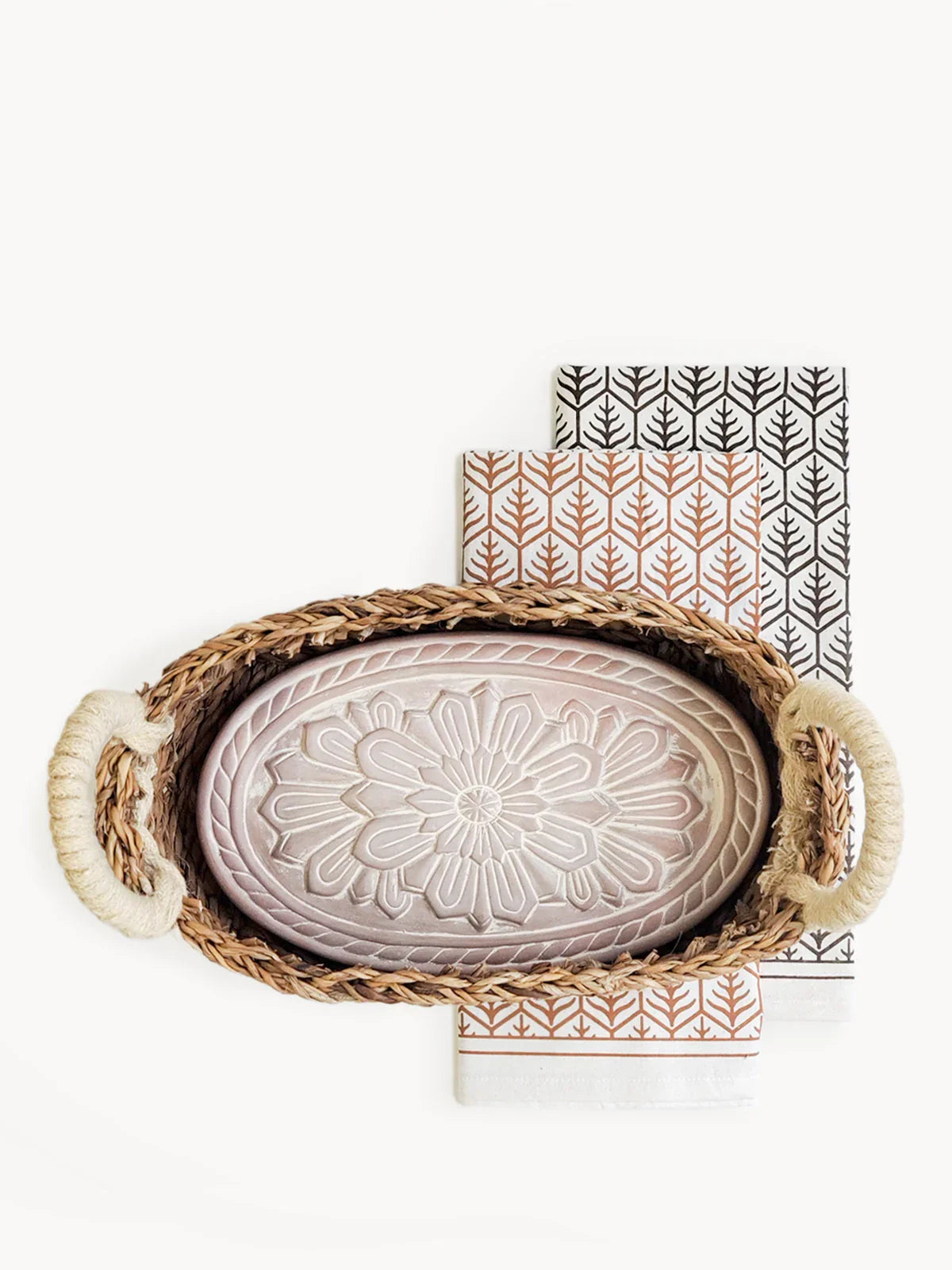 Woven bread warmer basket with floral carved ceramic lid on patterned tea towels