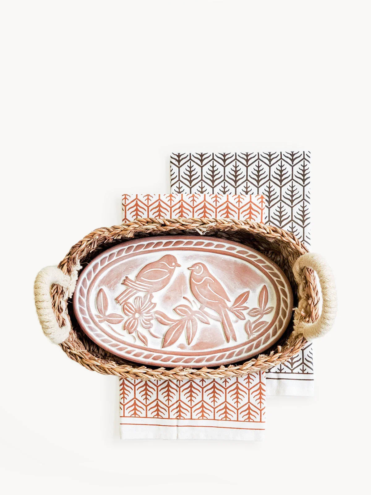 Oval terracotta bread warmer with lovebird design in woven basket on patterned tea towels