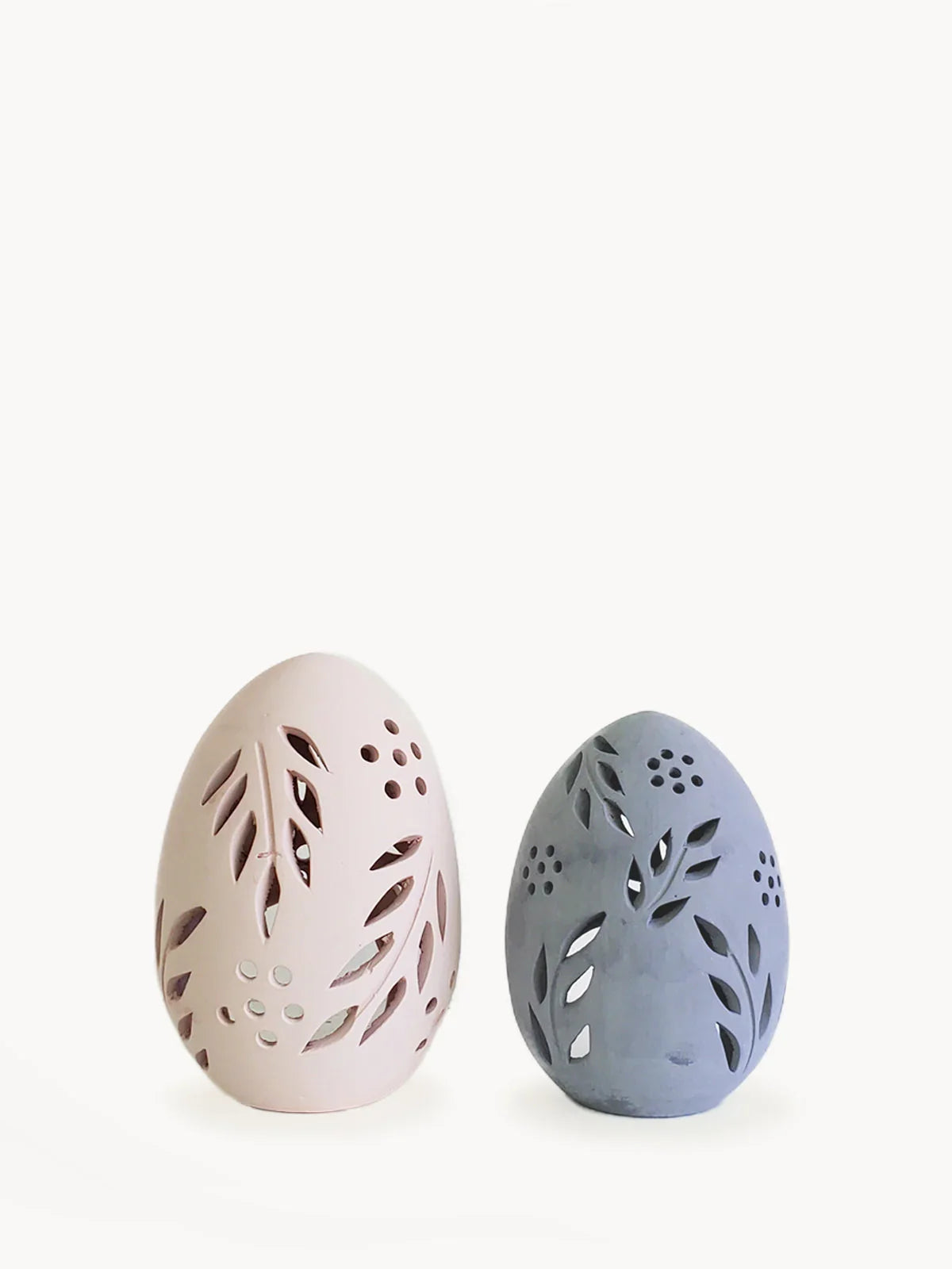 Pair of egg-shaped terracotta candle lanterns in blush pink and slate gray with leaf cut-out designs