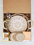 Gift box containing ceramic bread warmer with floral design, lemon cookies, herbal tea, coasters, and dried flowers