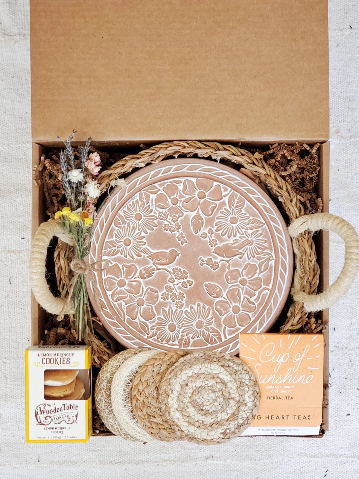 Gift box with floral embossed ceramic bread warmer, coasters, lemon meringue cookies, herbal tea, and dried flowers