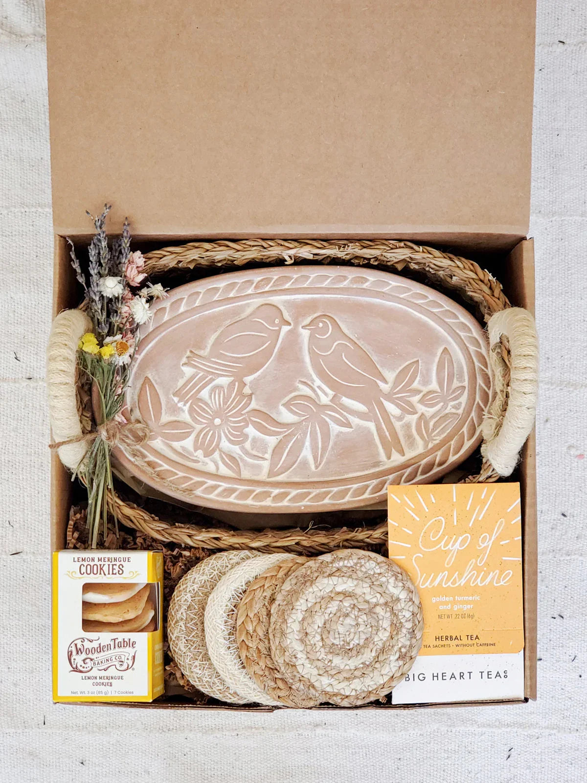 Gift box with oval bread warmer featuring lovebird design, herbal tea, lemon cookies, coasters, and dried flowers