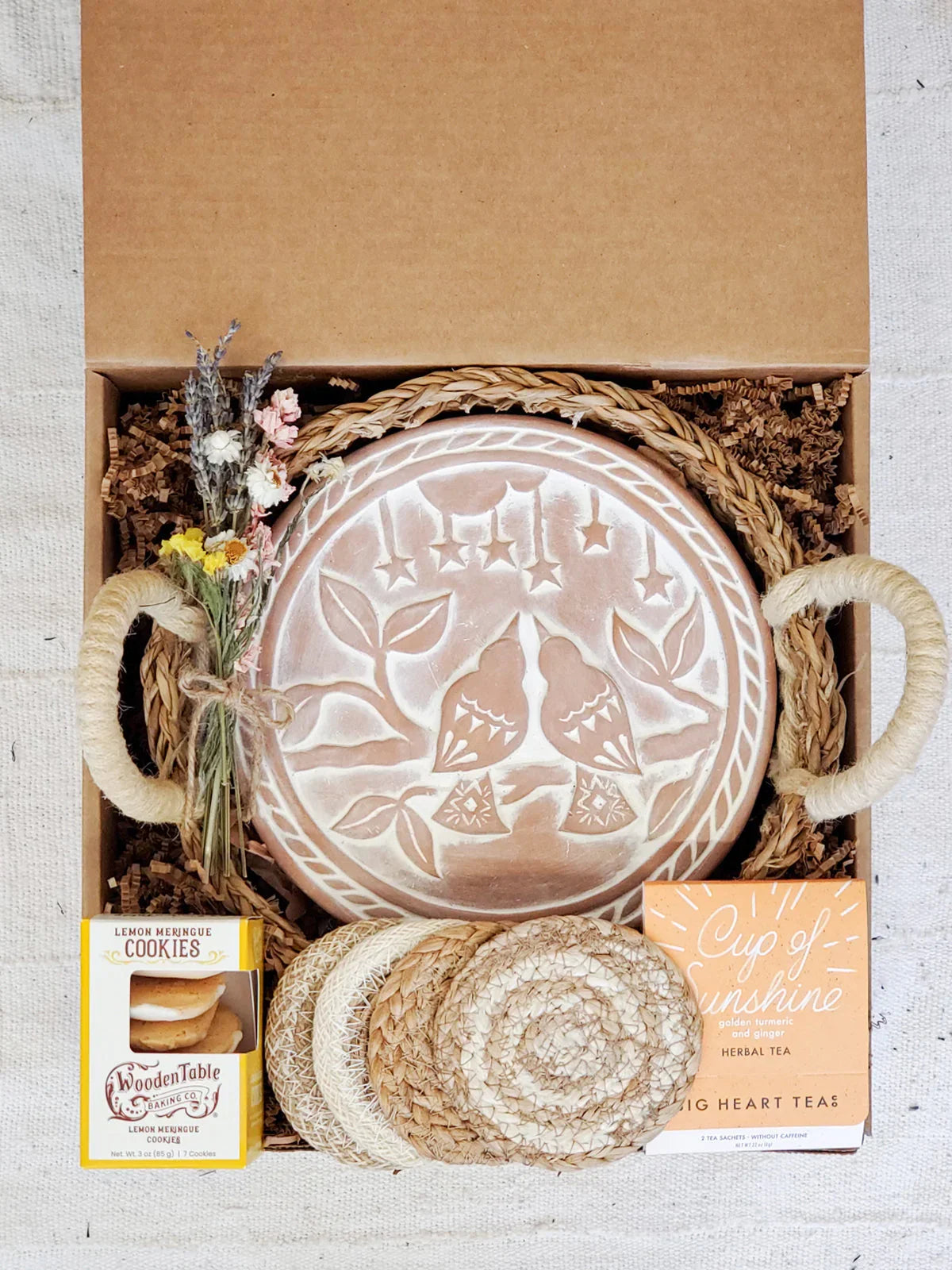 Gift box with lovebird round bread warmer, dried flowers, lemon meringue cookies, herbal tea, and woven coasters