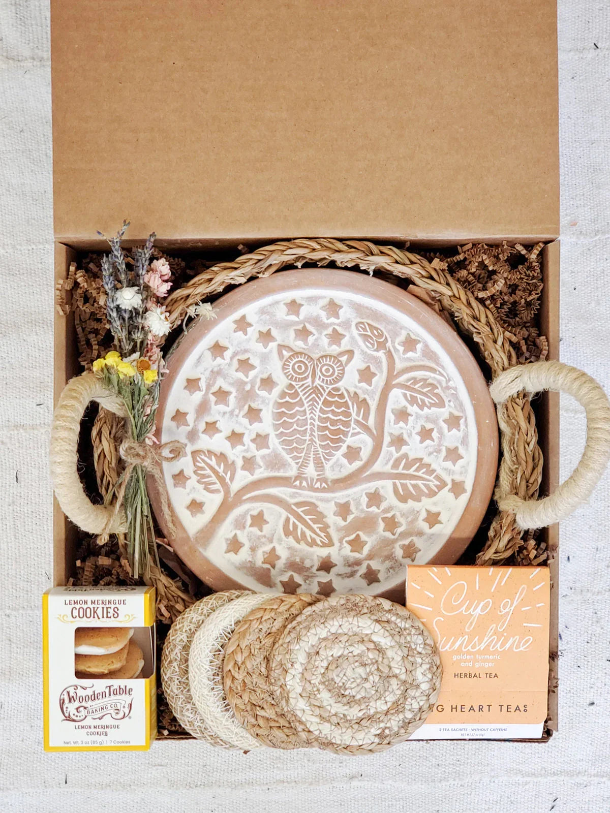 Gift box with owl-engraved bread warmer, lemon meringue cookies, herbal tea, coasters, and dried flowers