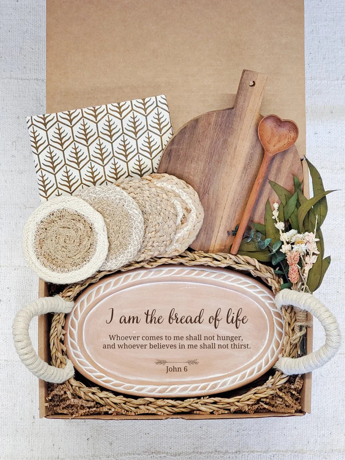 Decorative bread warmer gift box with biblical quote, wooden cutting board, coasters, heart-shaped spoon, and dried flowers