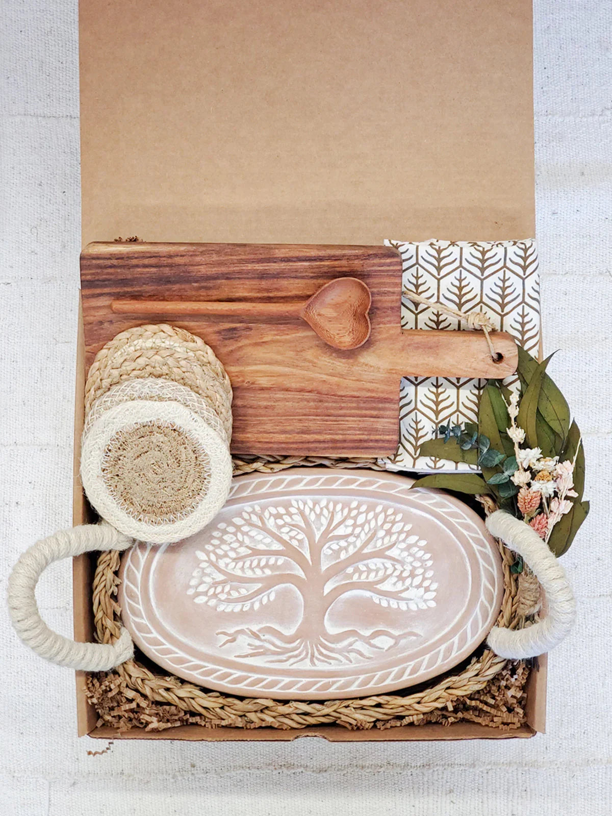 Gift box with carved tree bread warmer, wooden heart spoon, cutting board, coasters, and floral napkin