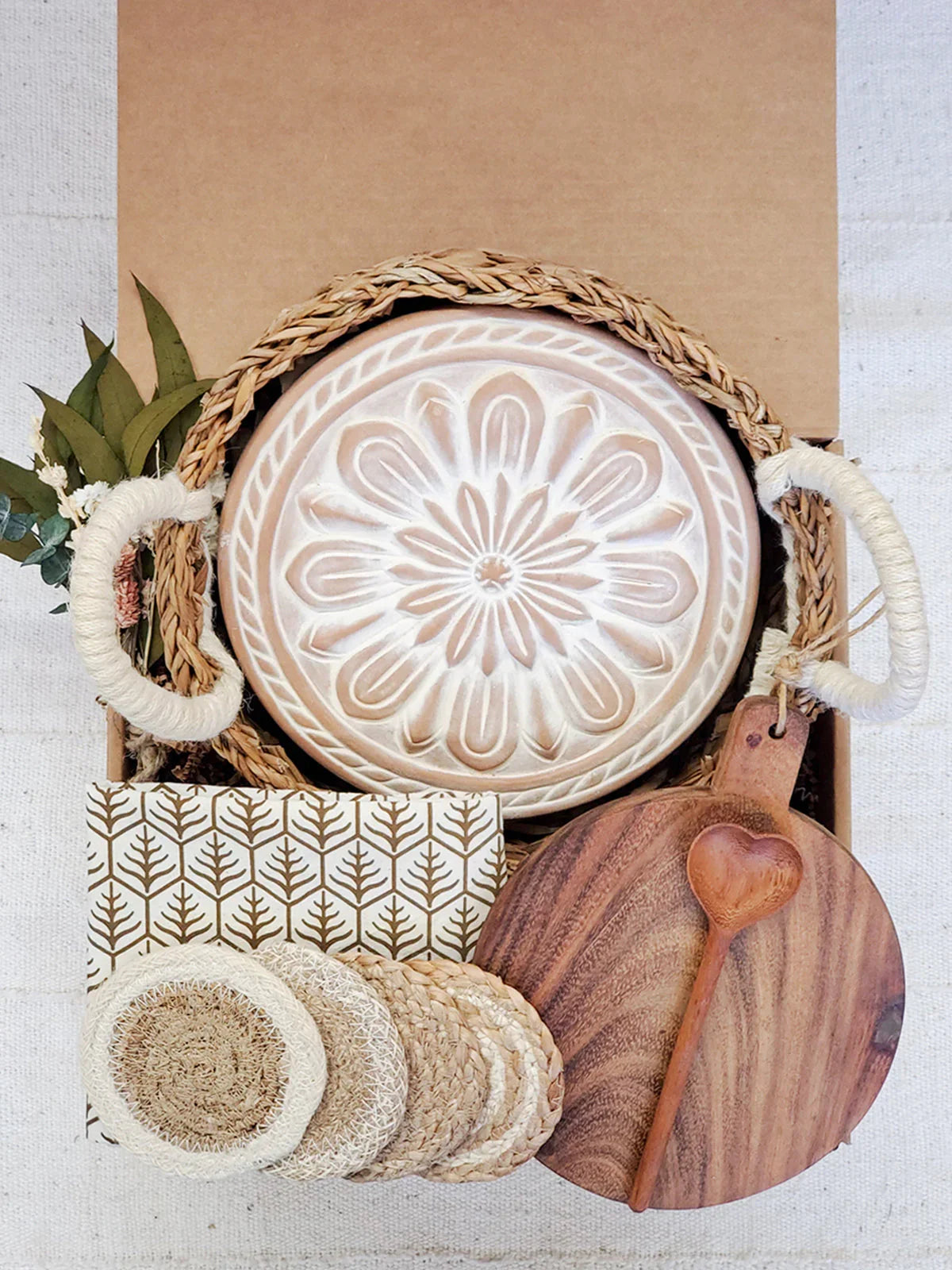 Round decorative ceramic bread warmer with woven basket, wooden cutting board, heart-shaped spoon, and coasters in gift box