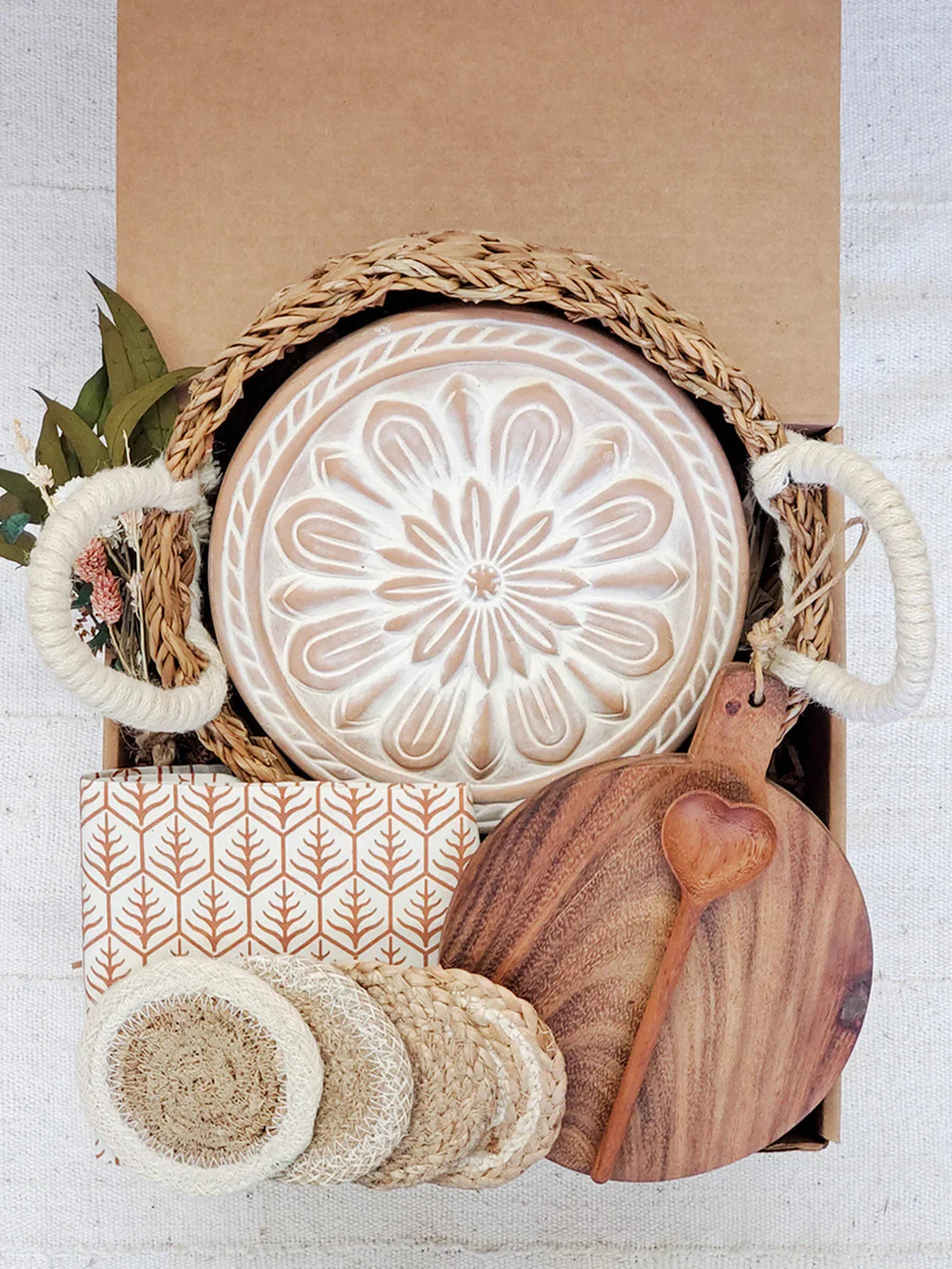 Round bread warmer with floral design in wicker basket, wooden cutting board, heart spoon, natural coasters