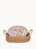 Handwoven basket with rope handles holding an oval ceramic plate embossed with two birds and floral design