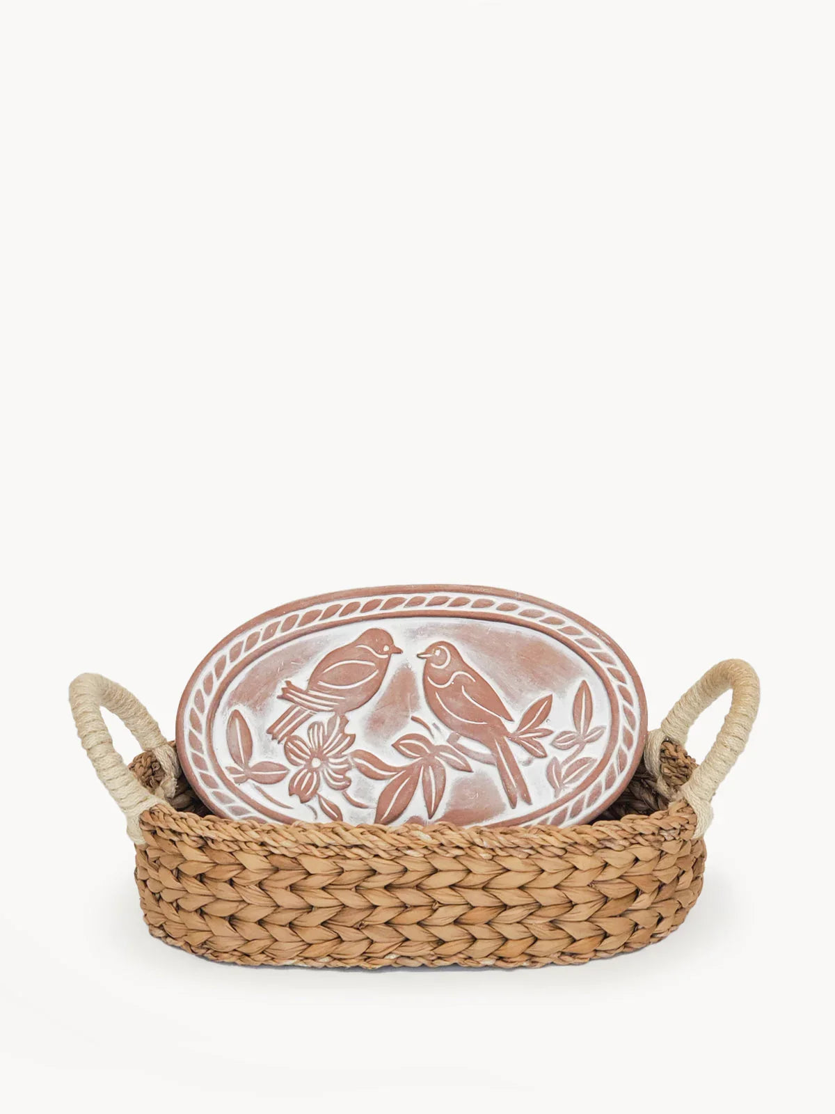 Handwoven basket with rope handles holding an oval ceramic plate embossed with two birds and floral design