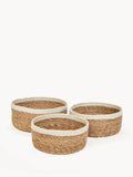 Set of three round, woven natural fiber storage bowls with white rim on white background