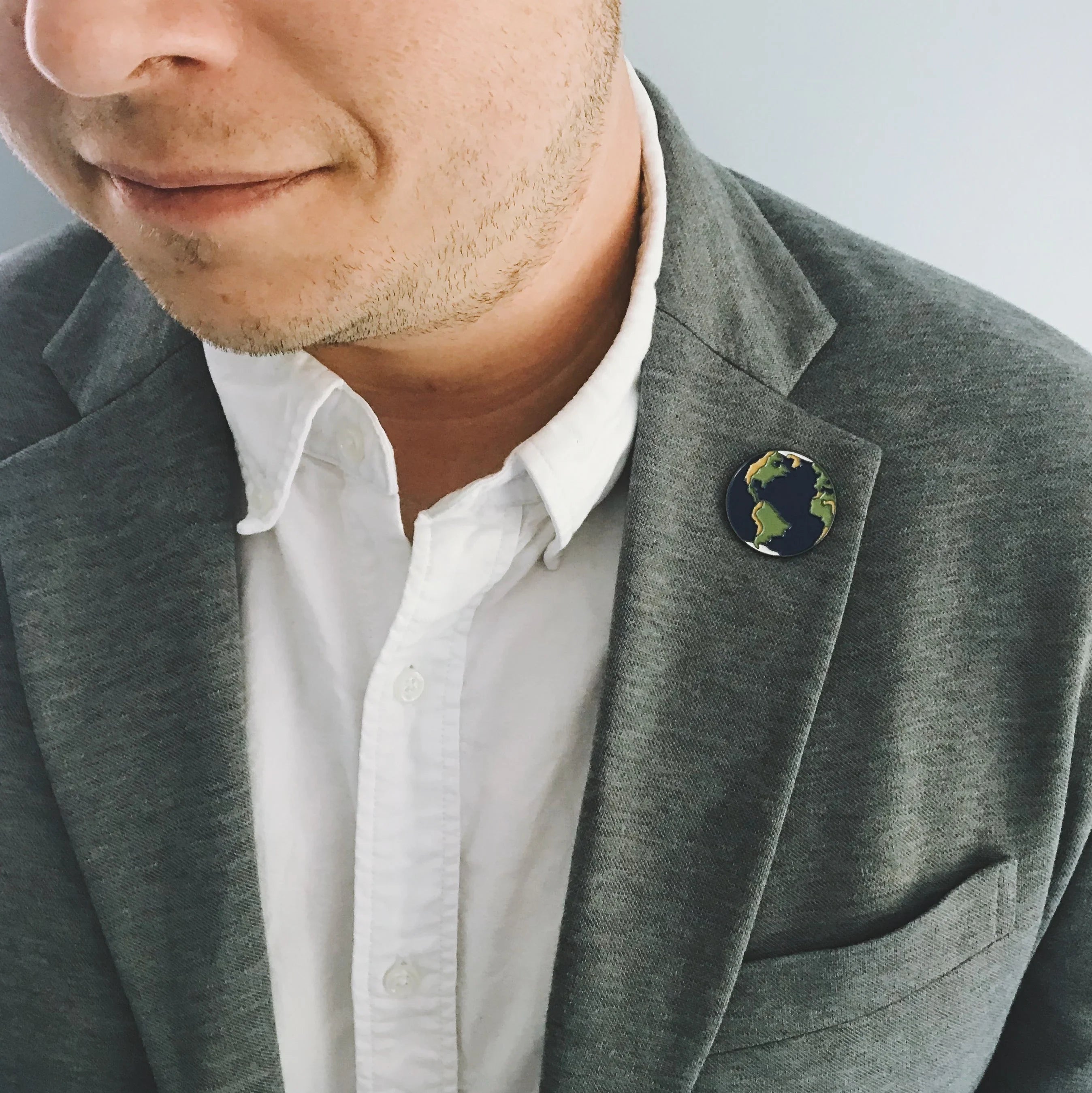Man wearing grey blazer and white shirt with Earth globe pin on lapel