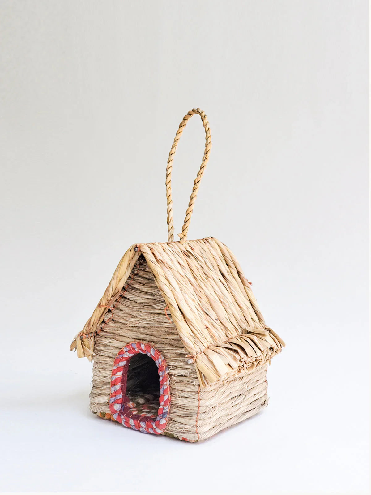 Handcrafted woven birdhouse cabin with a thatched roof and loop hanger on white background