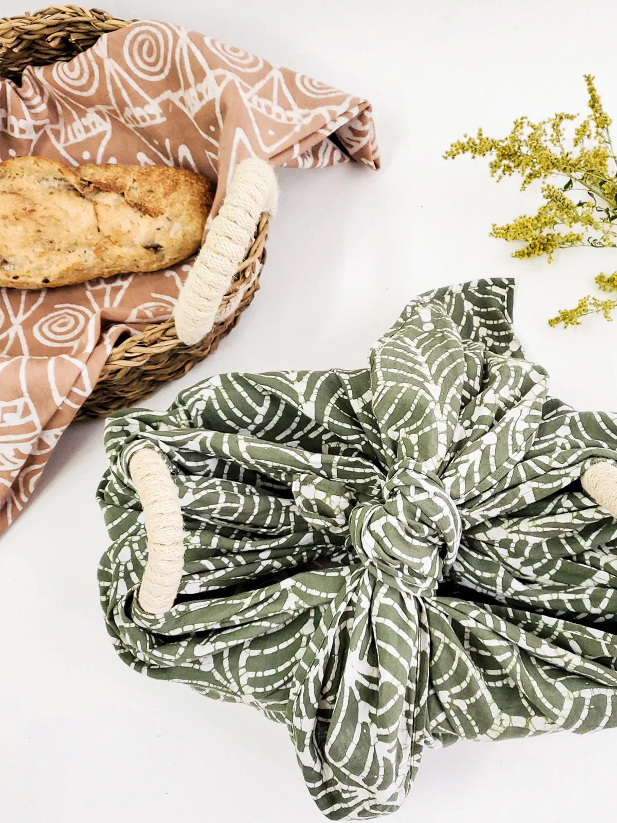 Oval woven bread warmer basket with patterned fabric liner and a loaf of rustic bread on white background