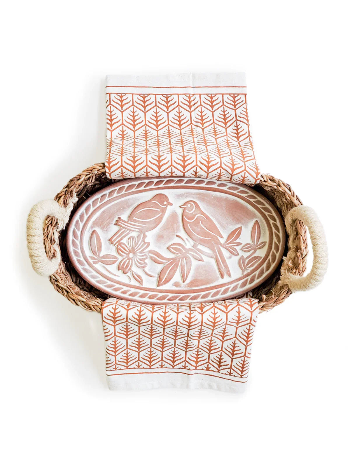 Woven basket with rope handles holding a terracotta breadwarmer featuring two lovebirds, accompanied by patterned orange and white tea towels