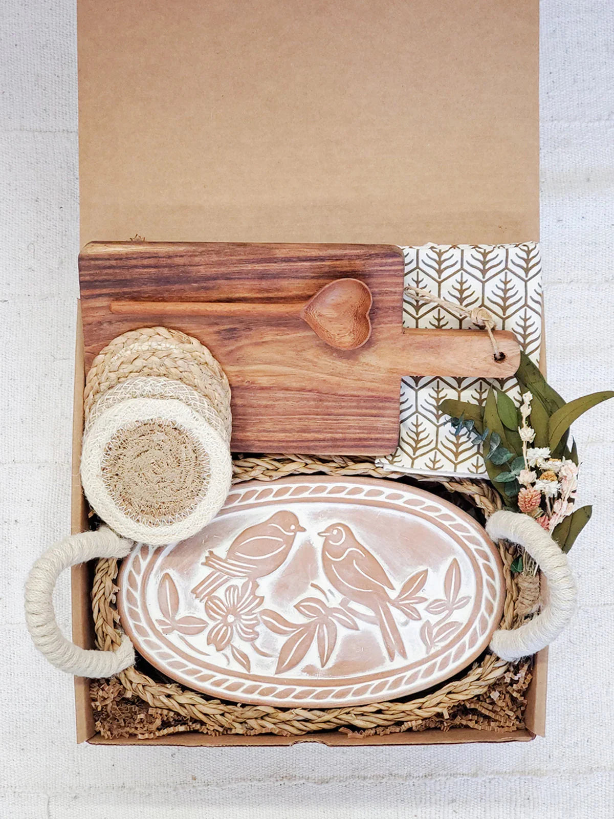Decorative gift box with carved wooden bread warmer, heart-shaped spoon, coasters, and dried flowers
