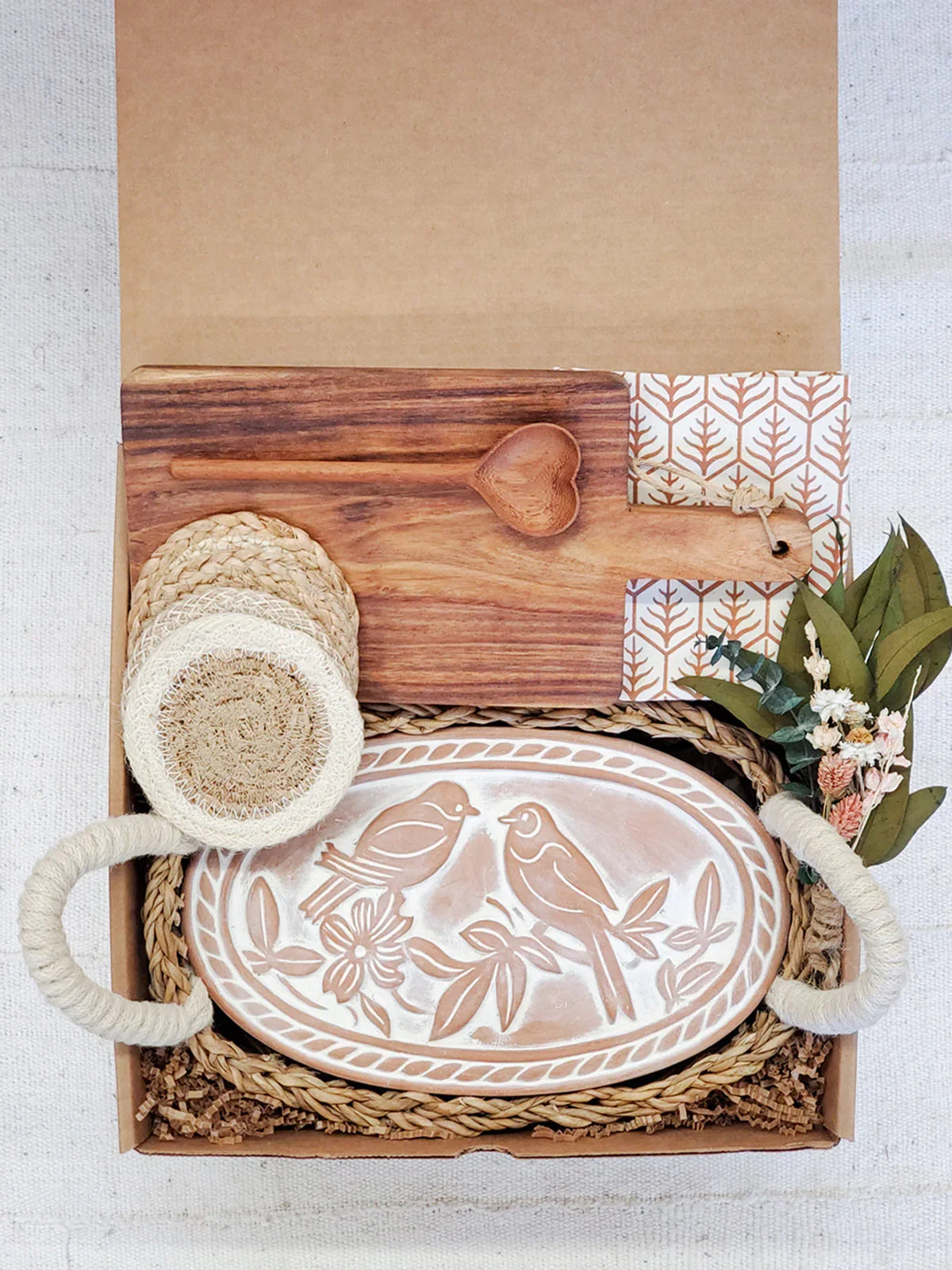 Gift box with woven coasters, wooden cutting board and spoon, ceramic bird platter with handles, dried flowers