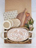 Gift box with rustic kitchen items including oval bread warmer with bird design, wooden cutting board, coasters, and dried flowers