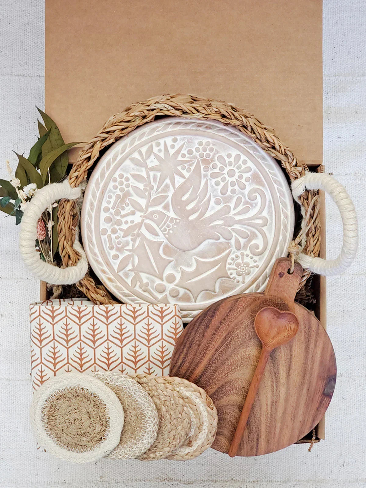 Gift box with round breadwarmer featuring bird design, woven basket, wooden heart spoon, coasters, and patterned cloth