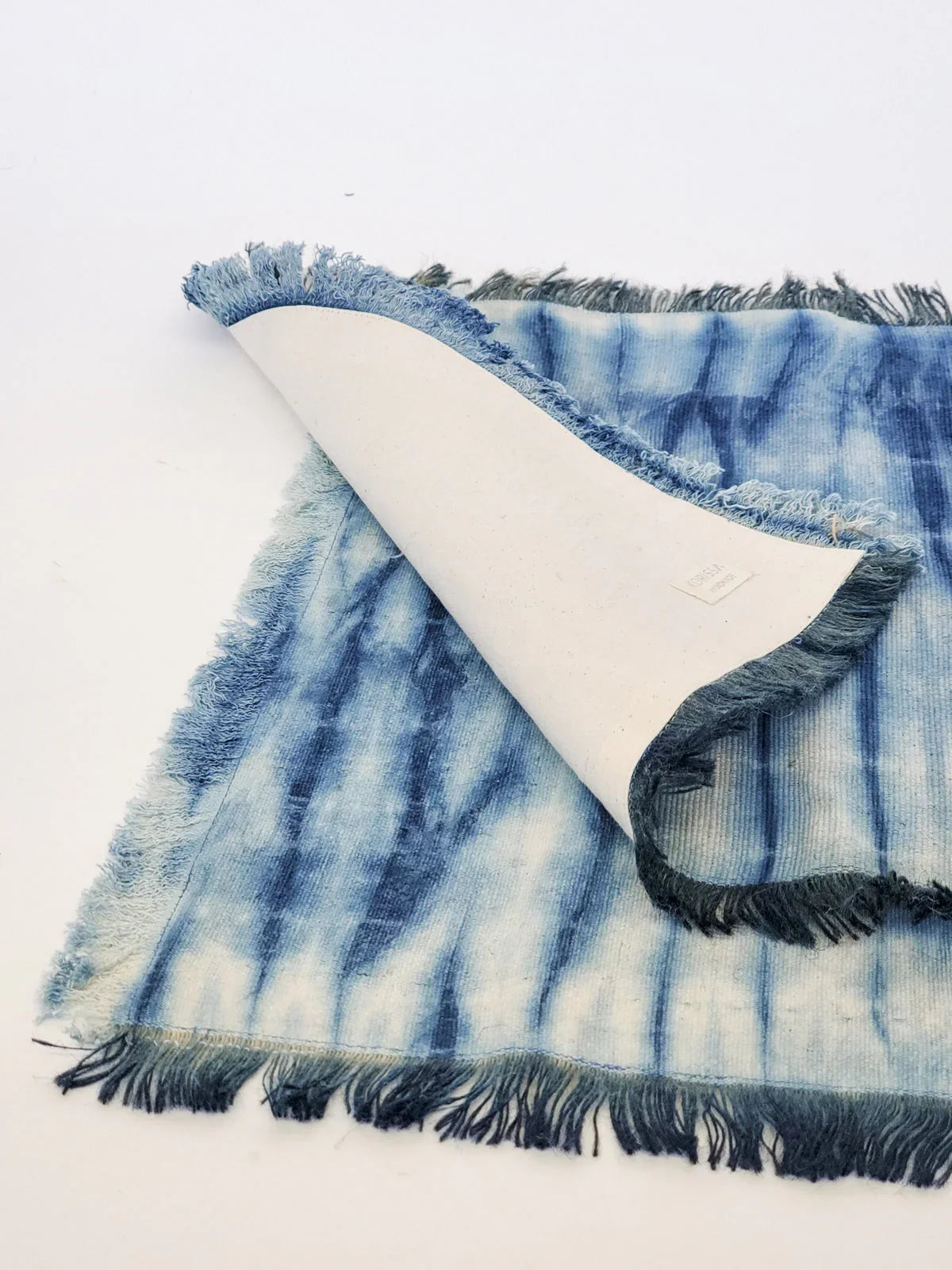 blue tie-dye cotton placemat with fringed edges on a white background