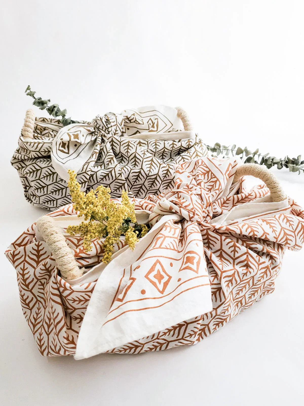 Two oval bread warmer baskets wrapped in patterned fabric with dried yellow flowers and eucalyptus