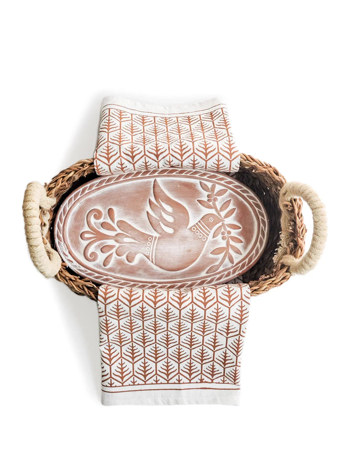 Woven bread warmer basket with a white and brown patterned cloth and a carved wooden board featuring a dove motif