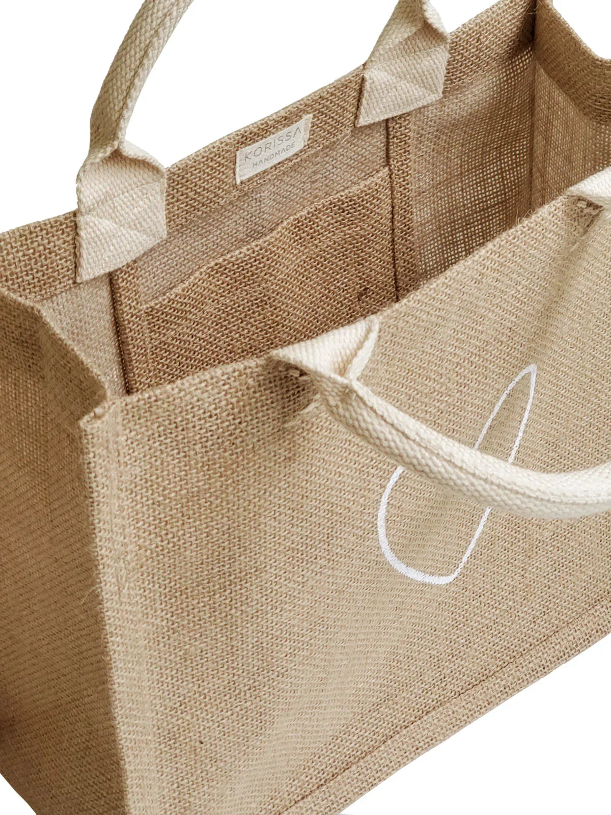 Beige woven jute tote bag with sturdy handles and white minimalist design, handmade by Korissa