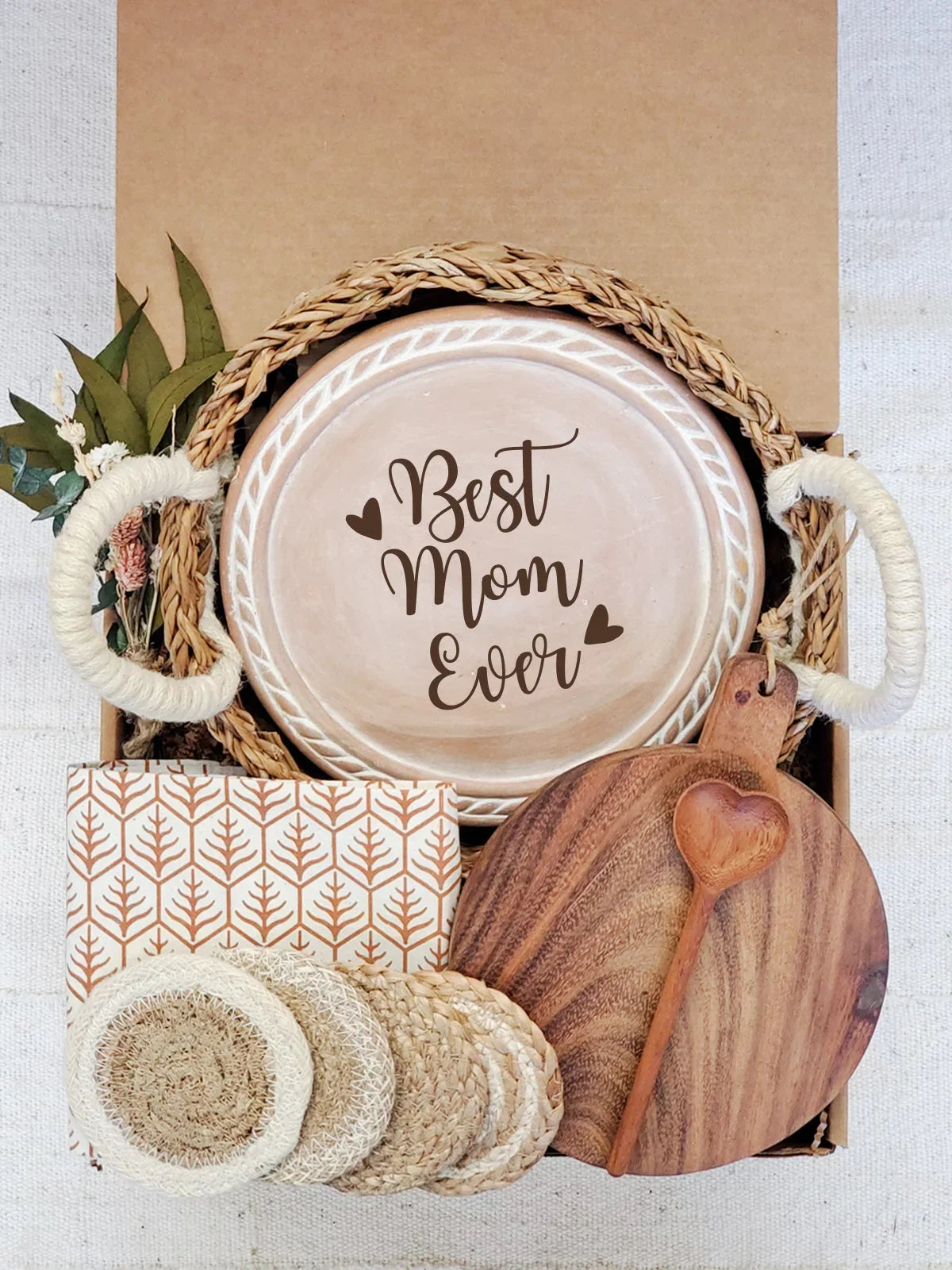 Gift box with woven bread warmer inscribed Best Mom Ever, wooden heart spoon, cutting board, coasters, and dried flowers