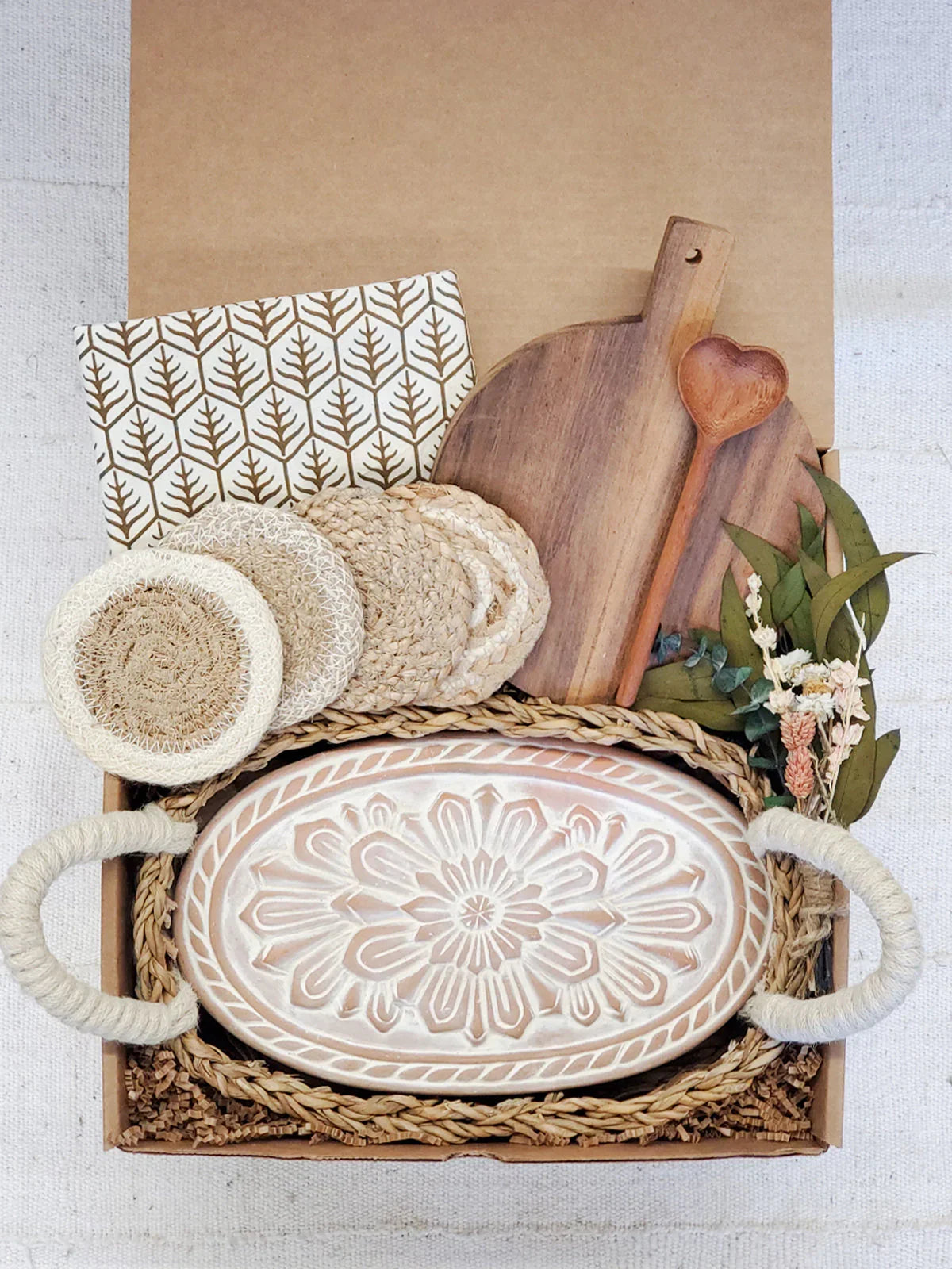 Gift box with decorative bread warmer, wooden cutting board, heart spoon, coasters, and dried flowers