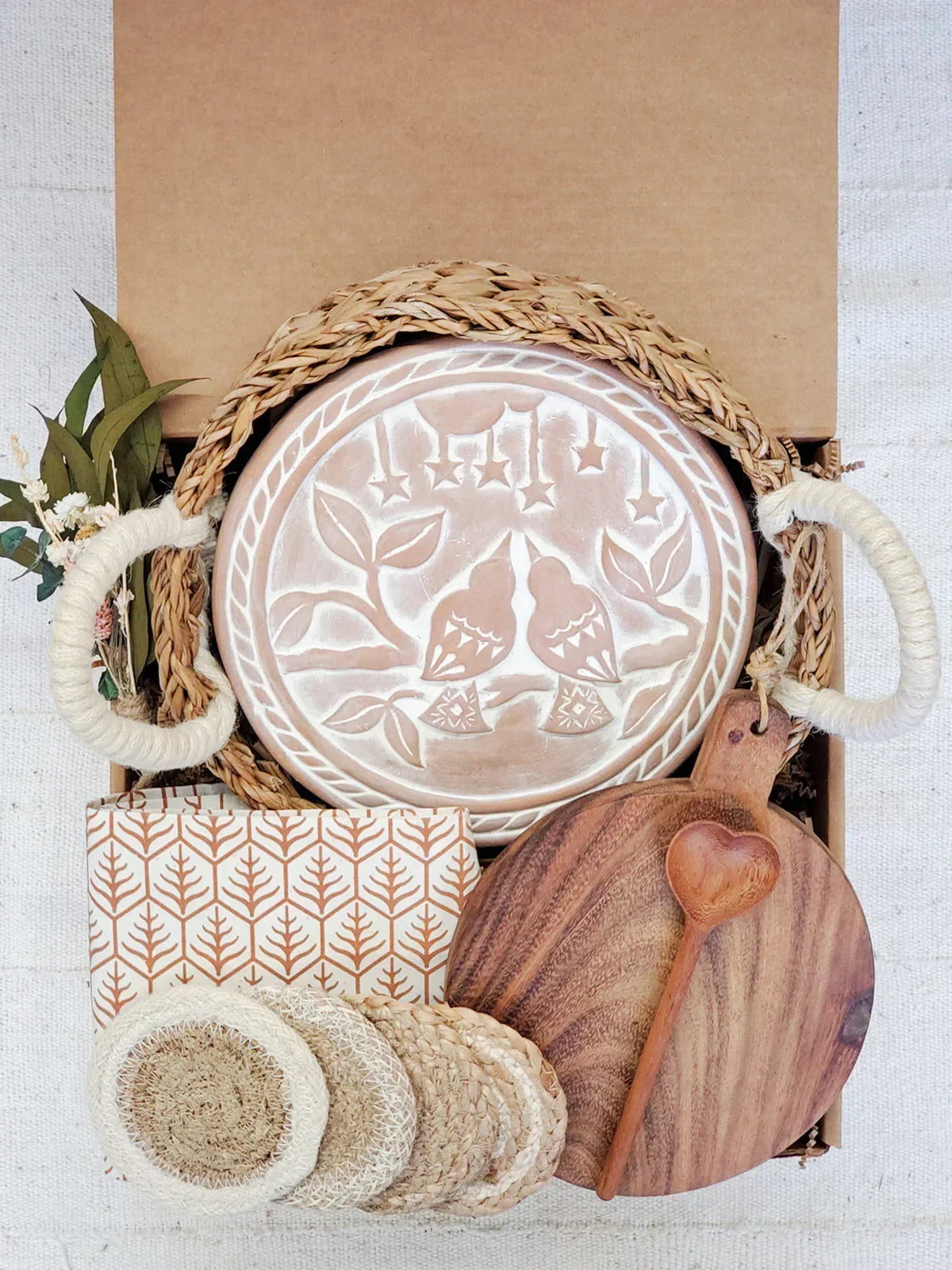 Gift box with round bread warmer featuring bird and star design, woven handles, wooden cutting board, heart-shaped spoon, and coasters