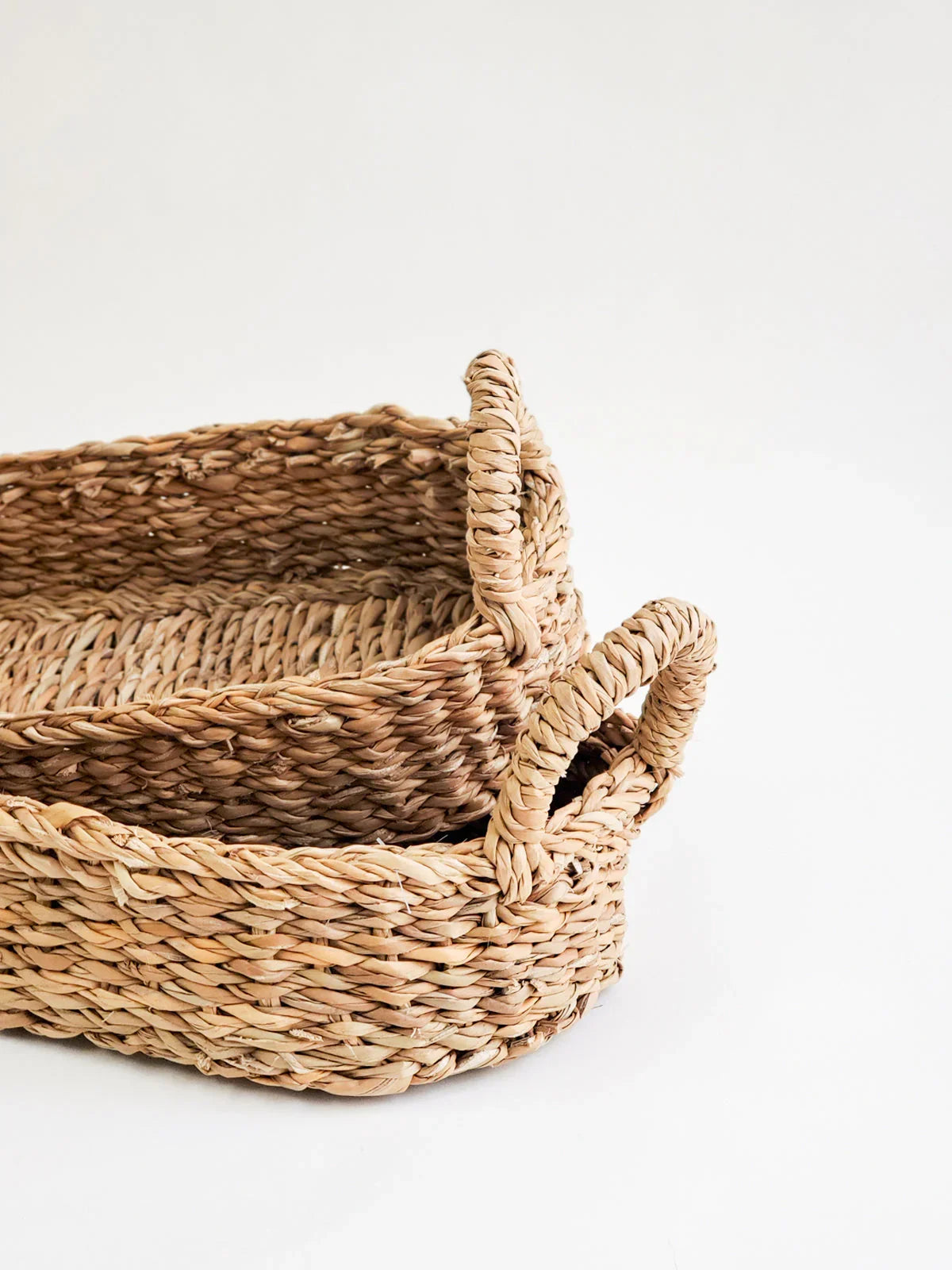Set of two woven bread baskets with natural handles on white background