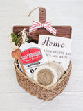 Woven gift basket with Soberdough bread mix, wooden spoon, coasters, floral decor, and home-themed towel