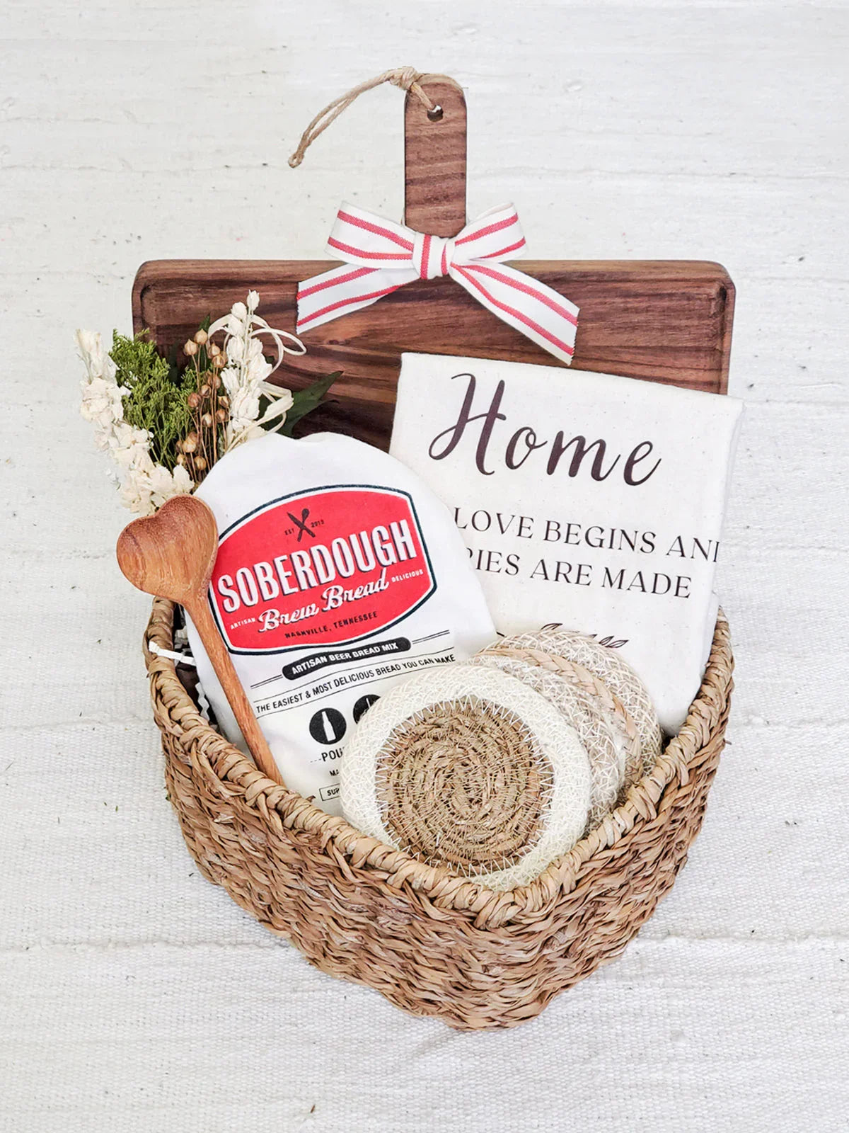 Woven gift basket with Soberdough bread mix, wooden spoon, coasters, floral decor, and home-themed towel
