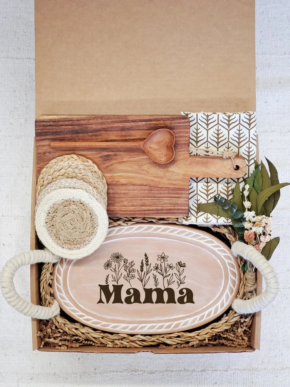 Gift box with wooden cutting board, heart-shaped spoon, coasters, floral napkin, and oval tray labeled Mama