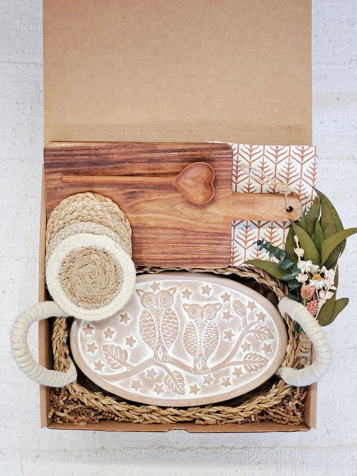 Oval bread warmer with owl design in woven tray, wooden heart spoon, and rustic coasters in gift box