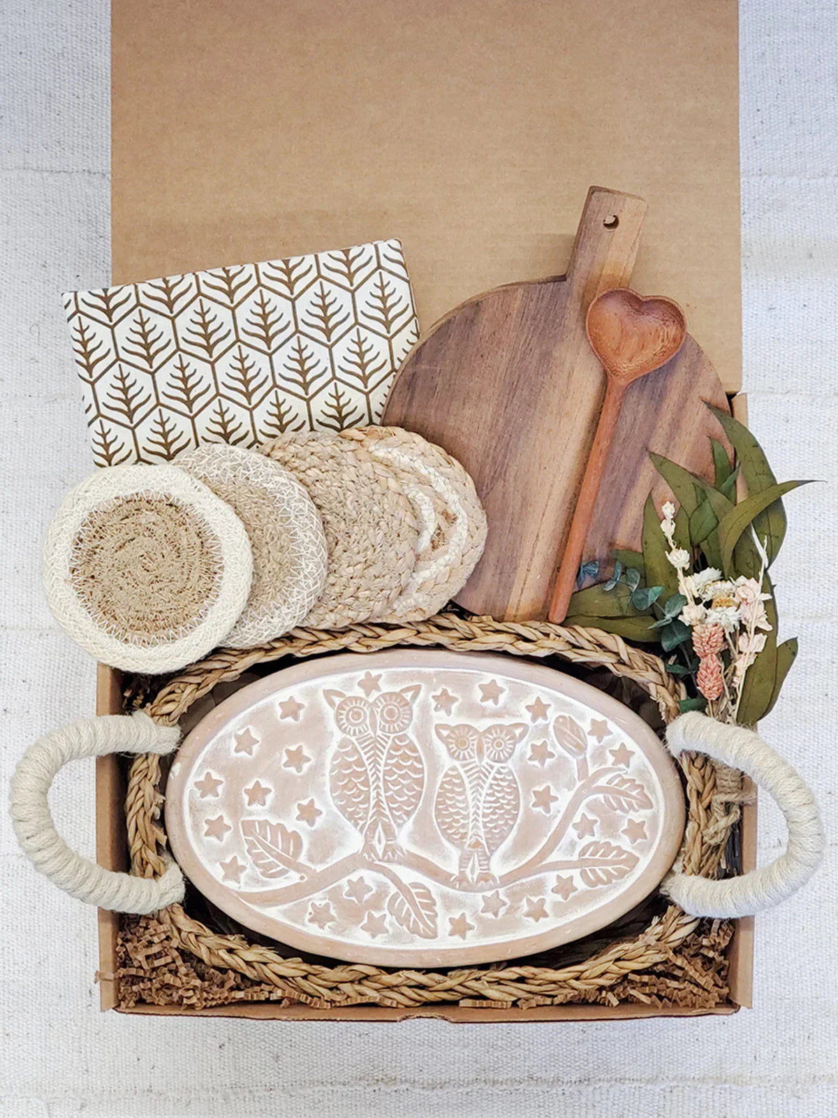 Gift box with owl design ceramic bread warmer, wooden heart spoon, cutting board, coasters, napkin, and dried flowers