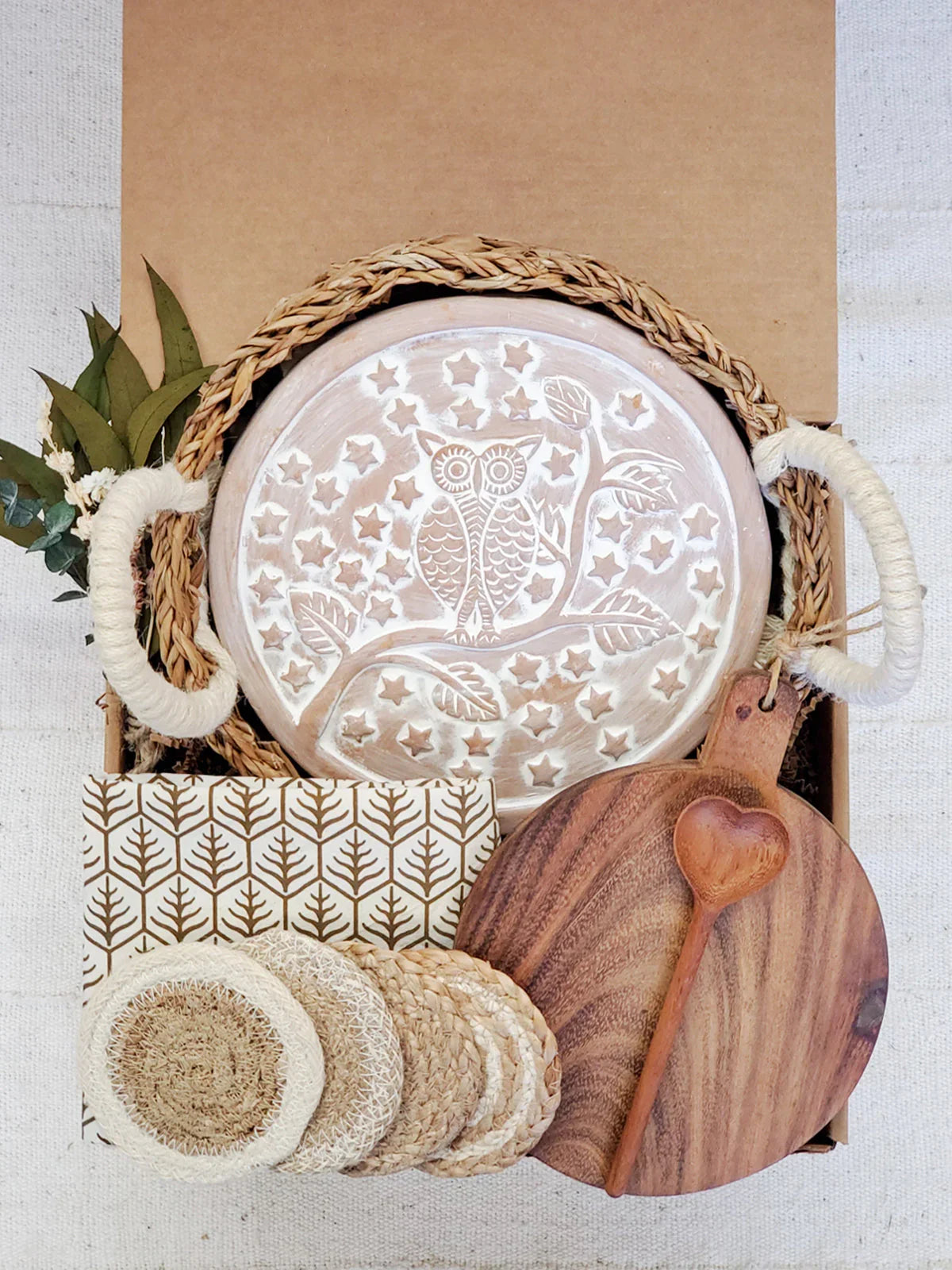 Gift box with woven bread warmer round owl design, wooden heart spoon, cutting board, coasters, and decorative leaves