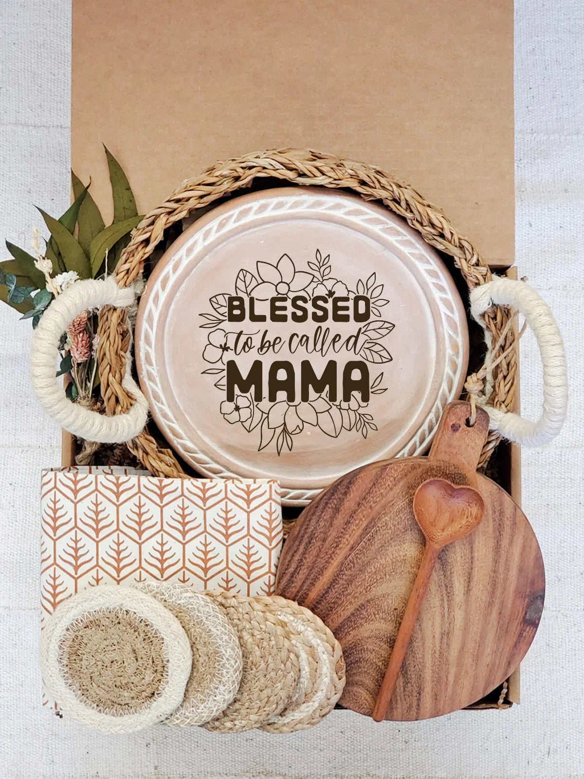 Gift box with woven handles holding a round ceramic plate reading 'Blessed to be called Mama', wooden heart spoon, coasters, and patterned napkin