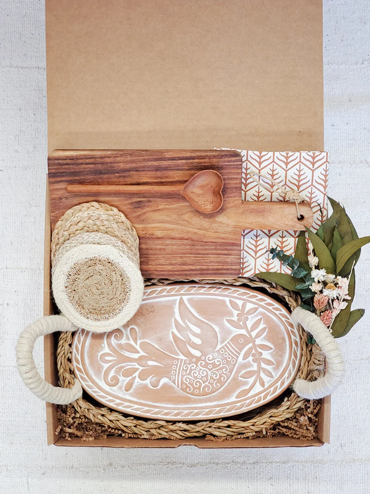 Rustic gift box with ceramic bird platter, wooden heart spoon, braided coasters, and greenery accents