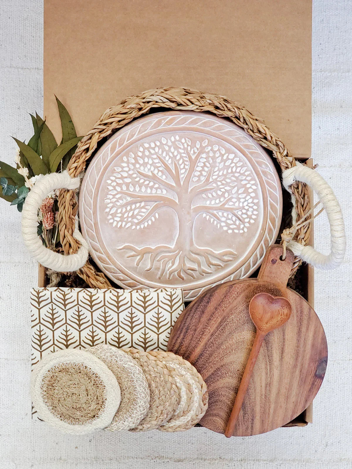 Decorative gift box with ceramic bread warmer featuring tree design, wooden cutting board, and coasters