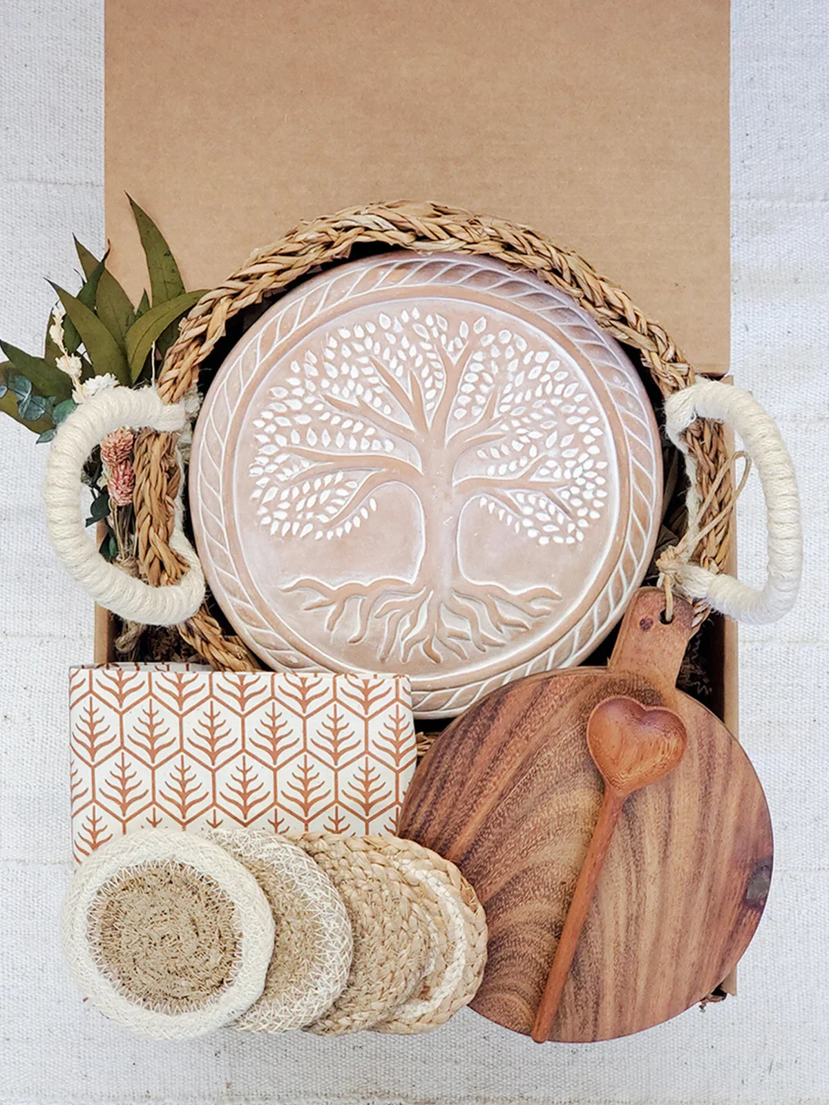 Gift box with woven handles, embossed tree bread warmer, wooden cutting board, heart-shaped spoon, coasters, and patterned napkin