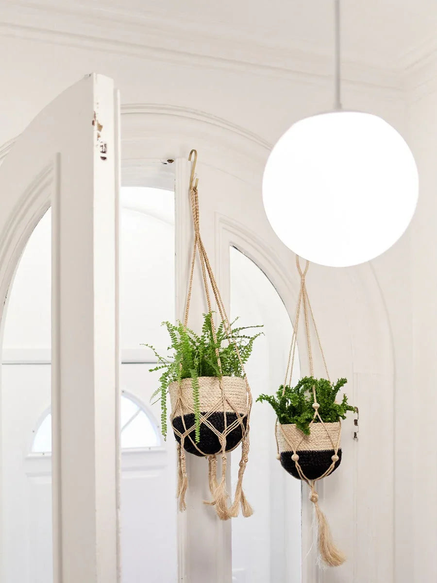 Two hanging woven planters with green plants in a bright white room with arched doorway and globe light