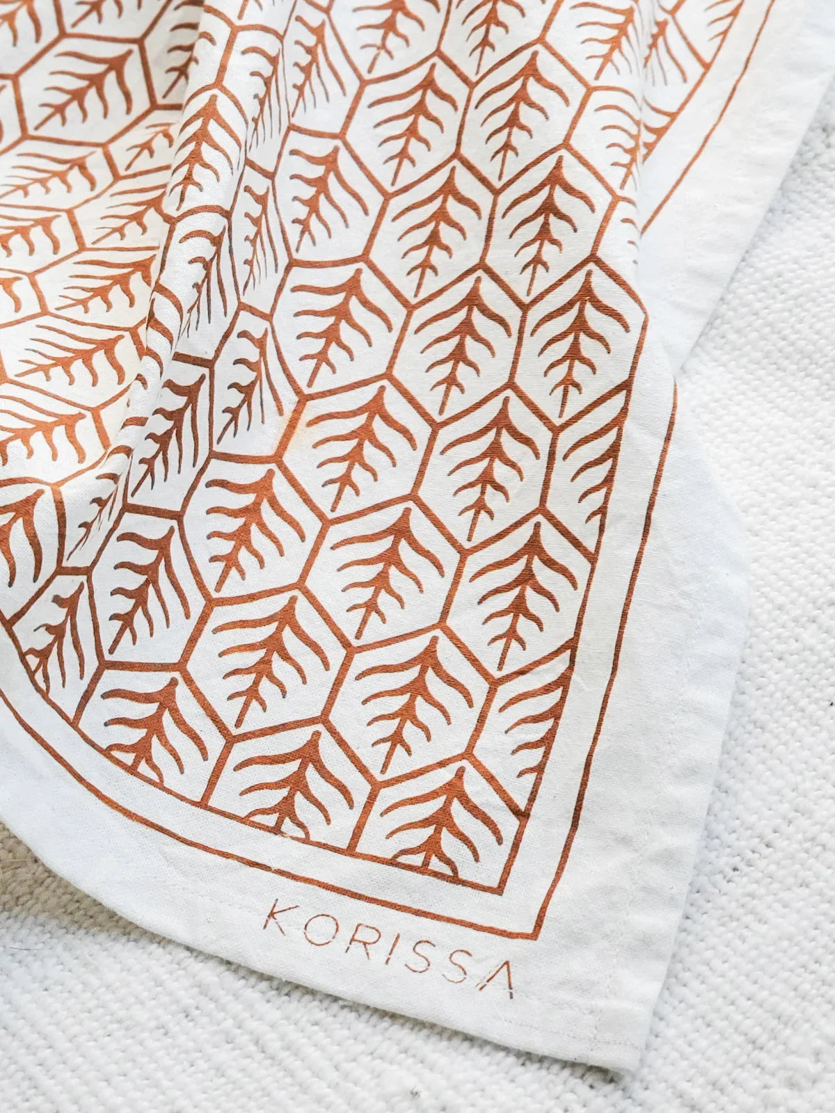 White kitchen tea towel with orange geometric tree pattern and Korissa branding on textured surface