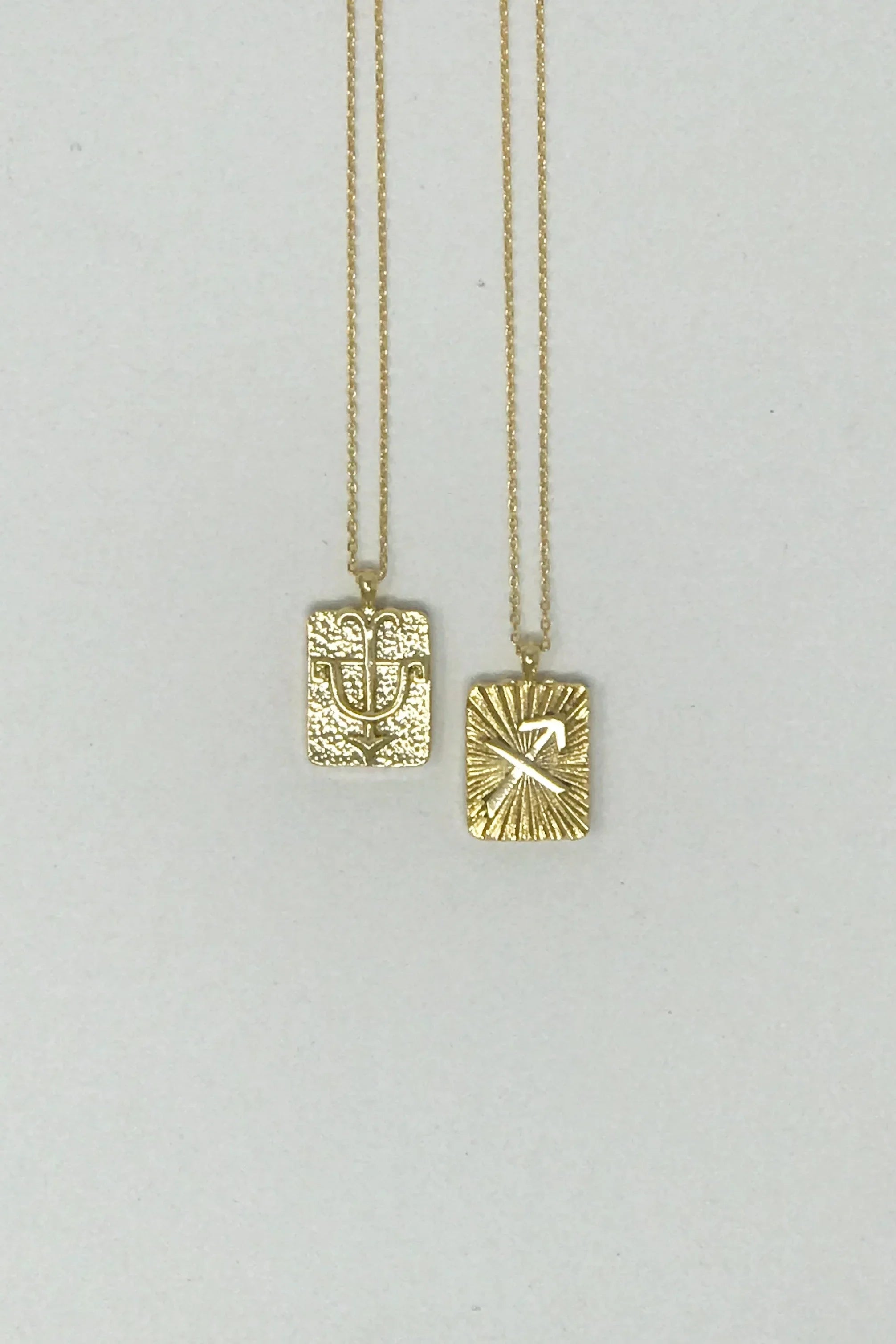 Two gold rectangular zodiac pendant necklaces on chains, featuring Sagittarius and Taurus signs