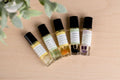 Five essential oil roll-on bottles labeled Grapefruit, Tea Tree, Lemongrass, Eucalyptus, and Lavender on a wooden surface