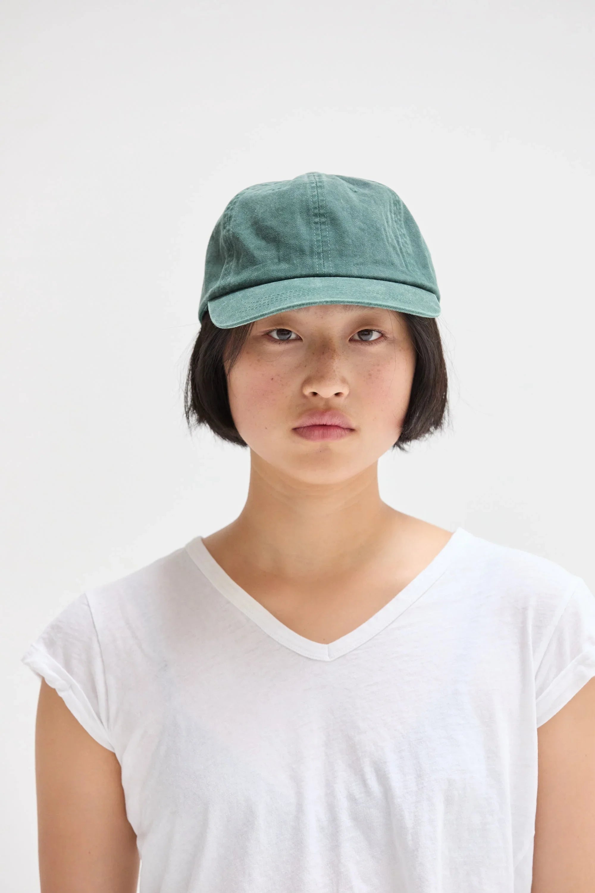 Woman wearing a green washed baseball hat and white V-neck tee, minimalist style